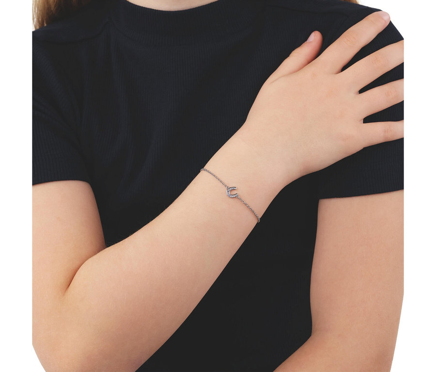 Nahaufnahme eines Arms, der ein silberfarbenes Kettenarmband mit einem halbmondförmigen Anhänger trägt, der mit kleinen Steinen verziert ist. Die Person trägt ein schwarzes Oberteil.