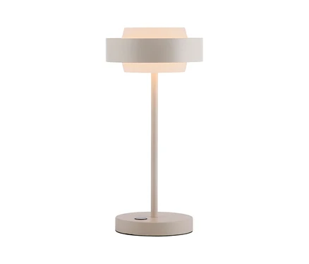 Eine hellbeige Tischlampe mit rundem Fuß, schlankem Stiel und geschichtetem Schirm. Der innere, durchscheinende Zylinder des Schirms leuchtet warm, umgeben von einem breiteren, undurchsichtigen Band. Ein kleiner Knopf ist am Fuß sichtbar.