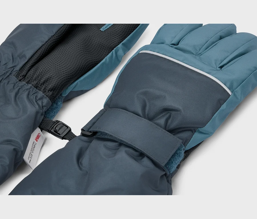 Ein Paar dunkelblaue und türkise Winterhandschuhe, verbunden durch eine schwarze Kunststoffschnalle. Der rechte Handschuh hat einen reflektierenden Streifen über den Knöcheln und einen Klettverschluss am Handgelenk. Ein "3M Thinsulate"-Etikett ist am linken Handschuh sichtbar.