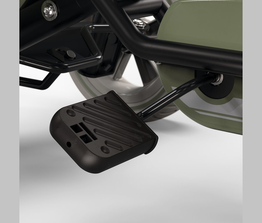 Nahaufnahme eines schwarzen, geriffelten Fußpedals, das mit dem grünen Korpus und dem schwarzen Rahmen eines Kinderfahrzeugs verbunden ist.