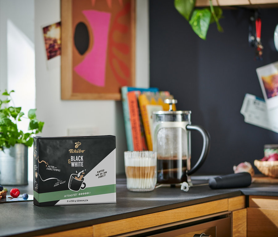 Eine Packung BLACK & WHITE - 2 x 250 g Gemahlen, eine French Press und ein Glas mit Kaffee stehen auf einer Küchentheke.