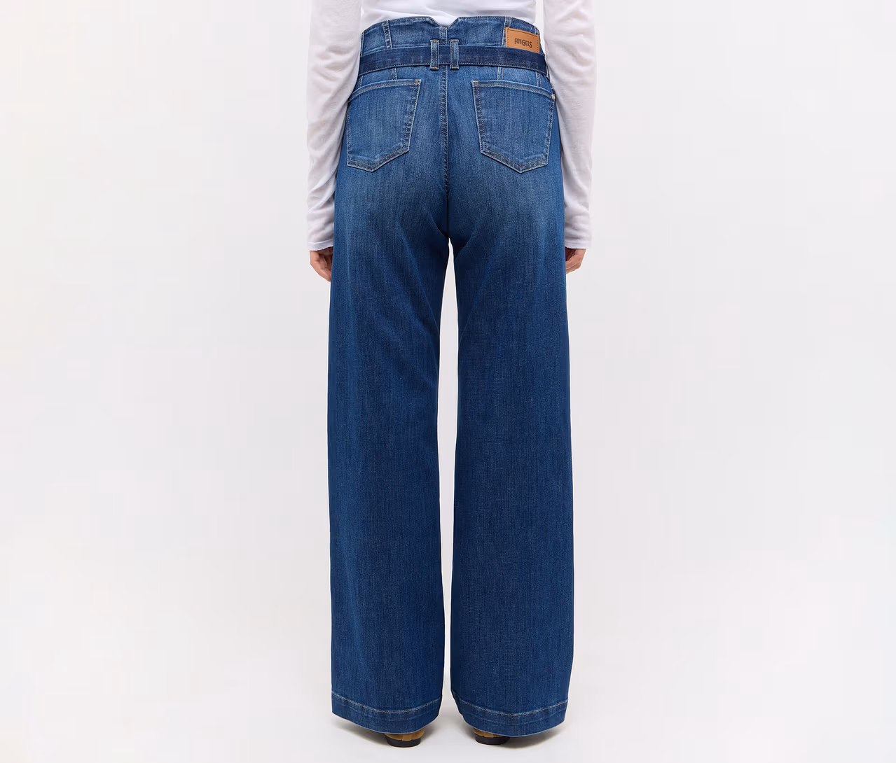 Person von hinten, trägt hochgeschnittene, weit geschnittene blaue Jeans mit Gürtel und ein weißes Langarmshirt.