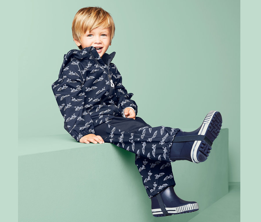 Junge sitzt in blauem Softshell-Overall mit Muster.