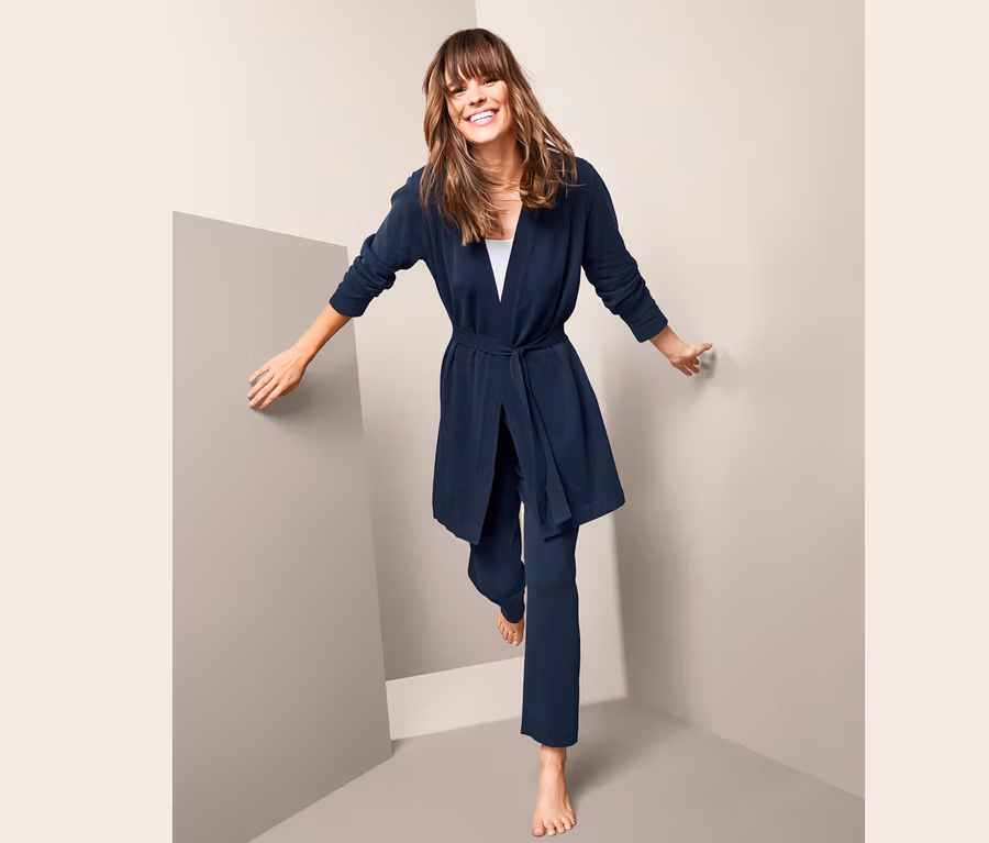 Frau in marineblauer Feinstrickjacke und Hose steht auf einem Bein.