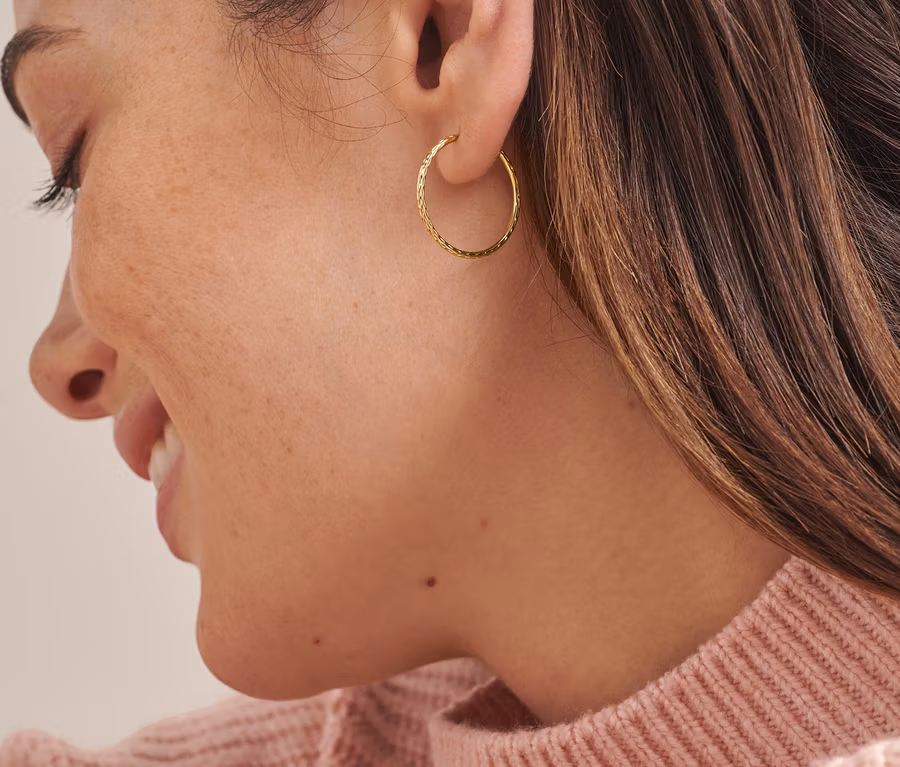 Detailaufnahme vom Gesicht einer Frau, die Gold-Creolen Basic flexibel trägt.
