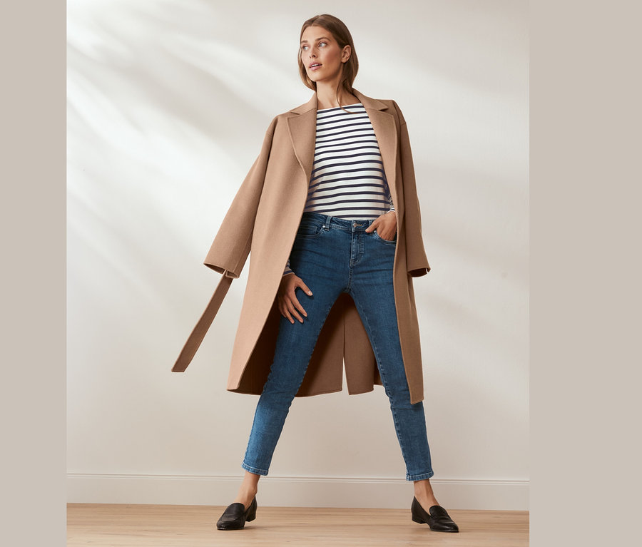 Frau posiert in Wollmantel mit Cashmere, blauen Jeans und Streifenshirt.