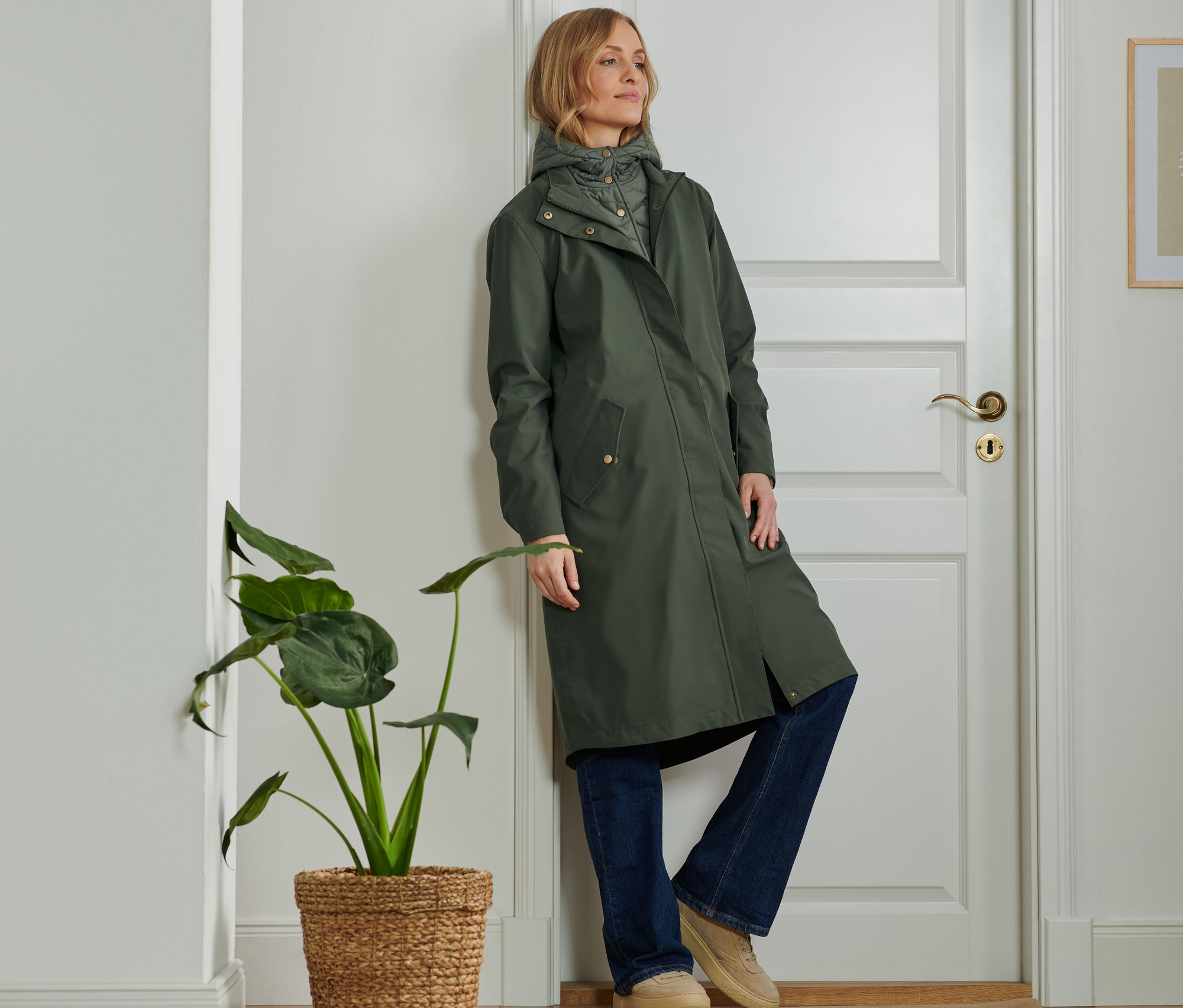 Frau lehnt an Tür und trägt einen 2-in-1-Outdoorparka.