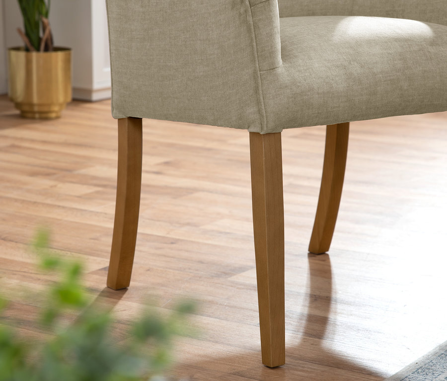 Detailaufnahme eines beigen Polsterstuhls mit Armlehne »Leopold« und Holzbeinen.