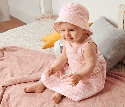 Ein Baby sitzt auf einem Bett und trägt ein Kleid mit passendem Hut.