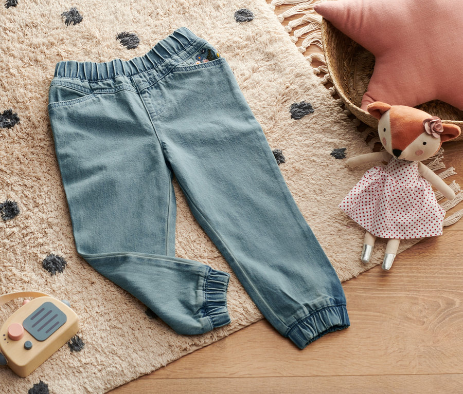 Denim-Schlupfhose liegt auf einem beigen Teppich mit schwarzen Tupfen.