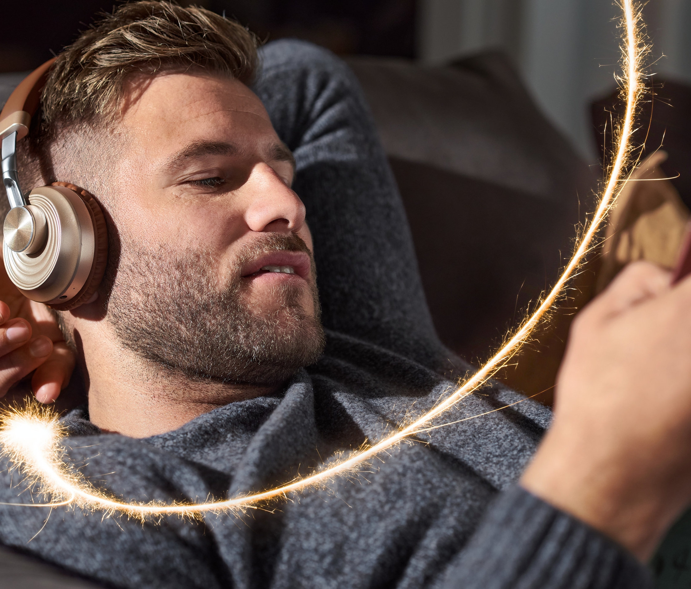 Mann liegt auf einer Couch und trägt On-Ear-Bluetooth®-Kopfhörer und schaut auf sein Handy.