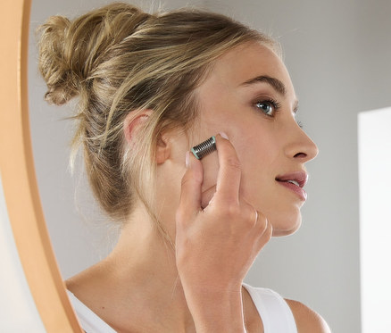 Frau verwendet Mini-Gesichtsepilierer vor Spiegel.