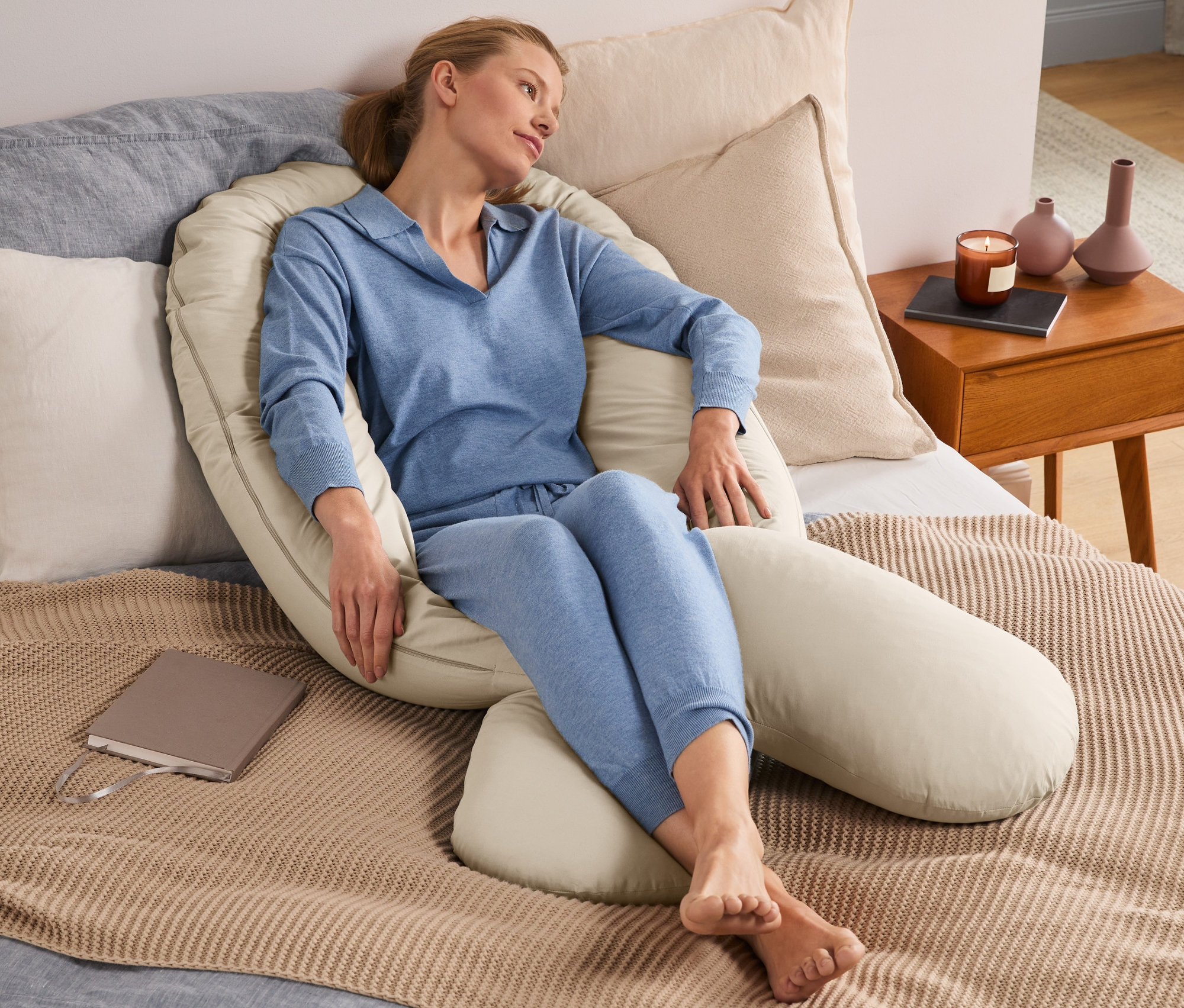 Frau sitzt im Bett, umgeben von einem XXL-Multifunktionskissen.