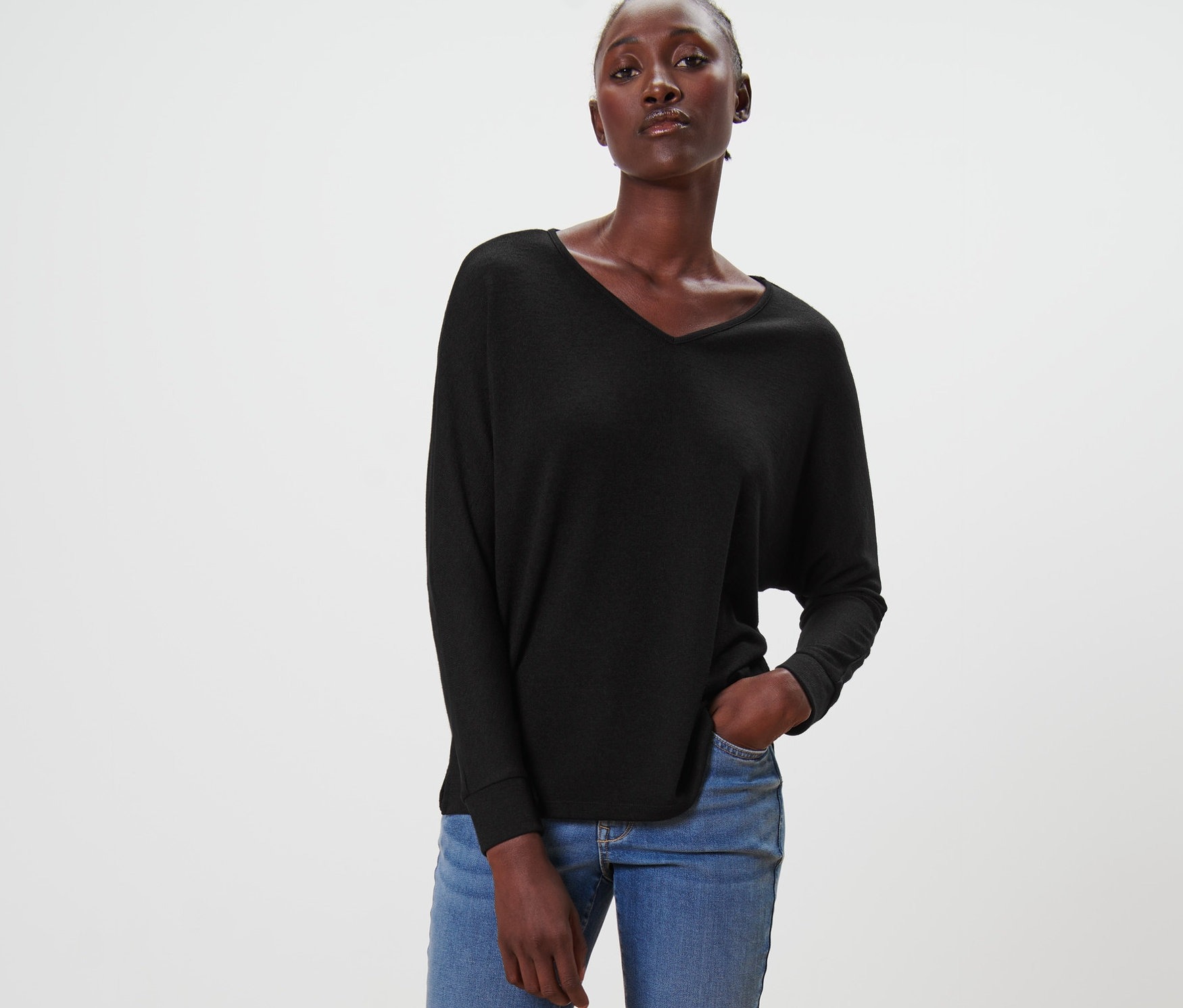 Frau posiert in schwarzem Fledermausshirt, Jeans und Loafern.