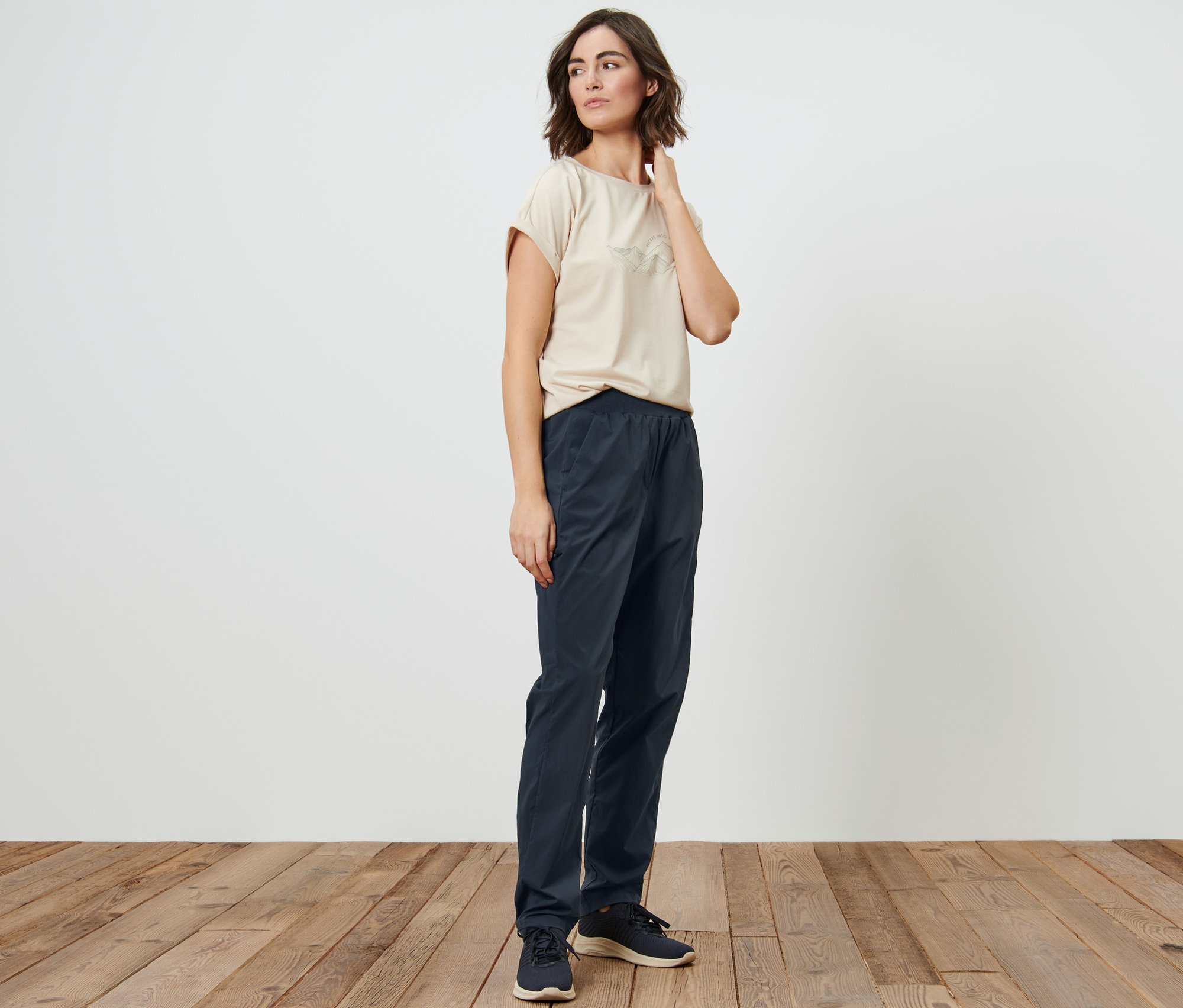 Frau posiert in einem beigen T-Shirt und einer dunkelblauen Funktionswanderhose.