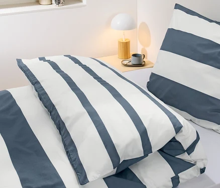 Detailansicht von gestreifter Perkal-Bettwäsche in Normalgröße auf einem Bett.