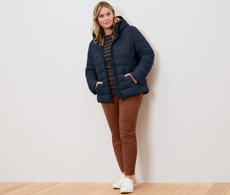 Frau posiert in dunkelblauer Steppjacke mit Kapuze, gestreiftem Shirt mit 3/4-Arm und cognacfarbener Stretchhose.