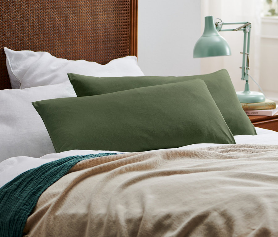 Zwei grüne Jersey-Kopfkissenbezüge liegen auf einem Bett mit einer beige Decke.
