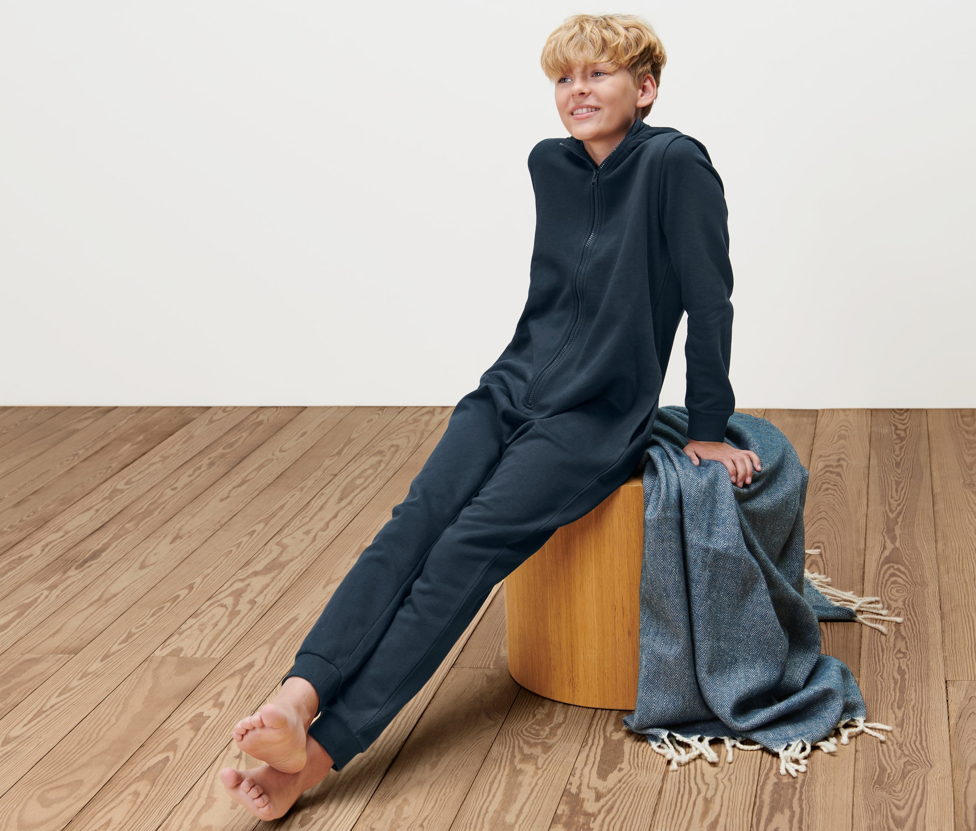 Ein Junge sitzt auf einem Hocker und trägt einen marineblauen Kinder-Lounge-Overall.