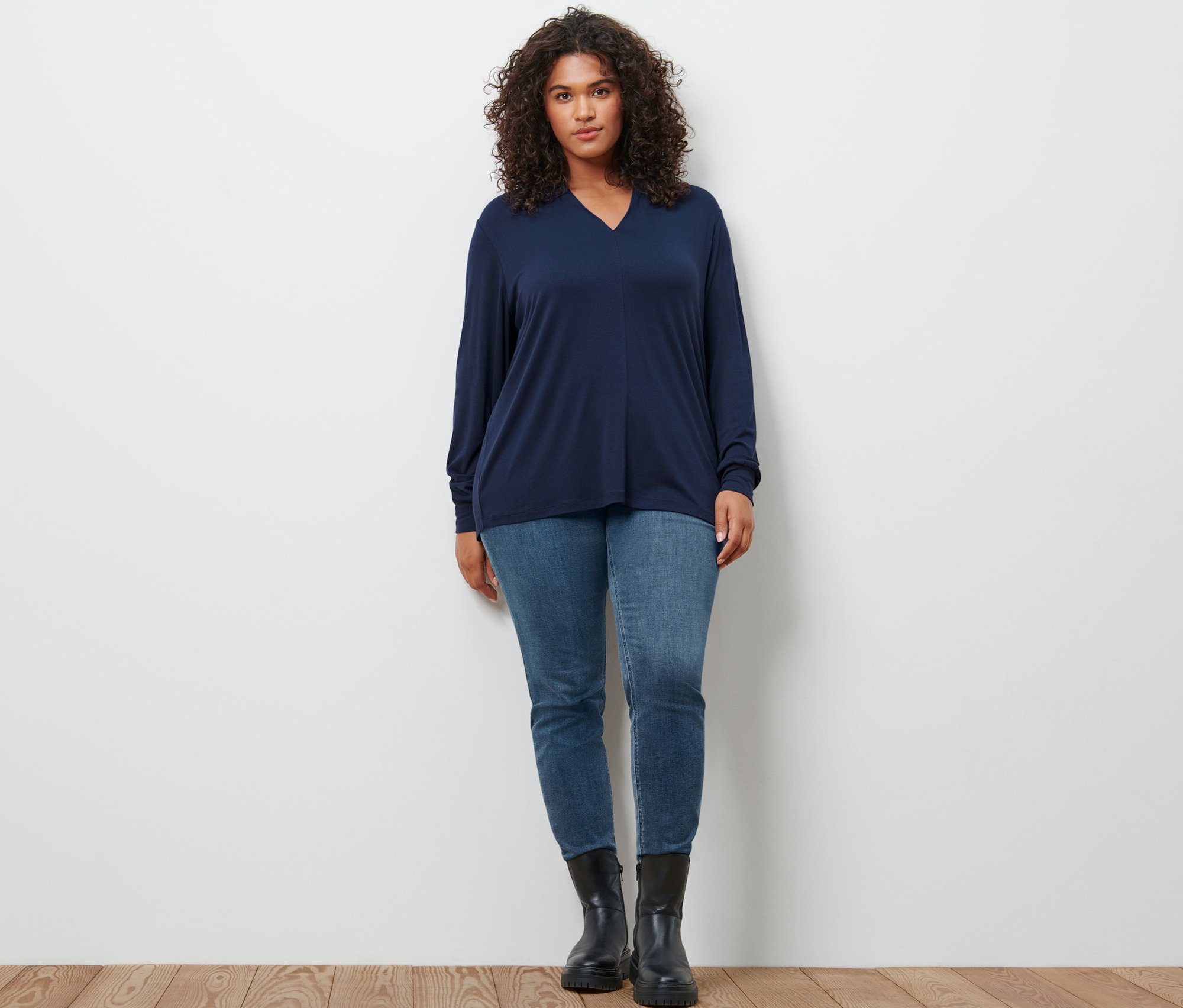 Eine Frau posiert in einem dunkelblauen Langarmshirt mit V-Ausschnitt, einer hellblauen Slim-Denim »Fit Emma« und Leder-Boots.