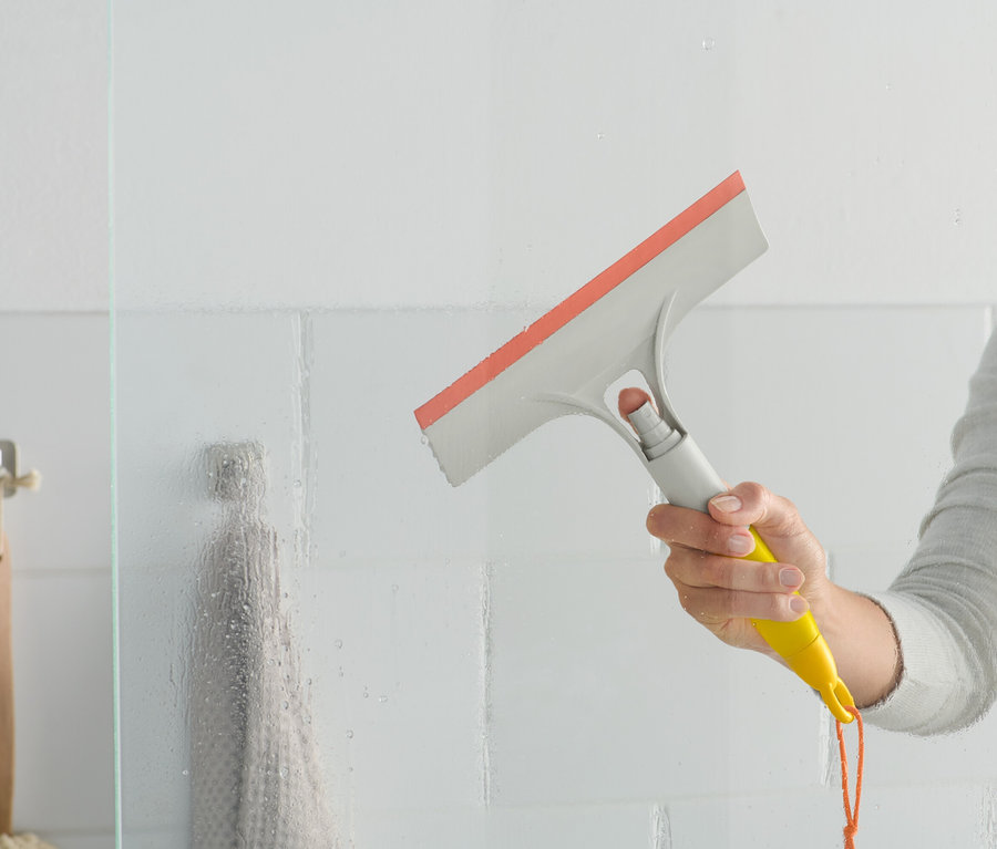 Eine Frau benutzt einen 3-in-1-Fensterwischer an einer gläsernen Duschwand.