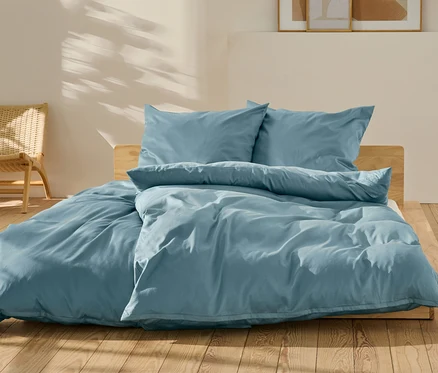 Blaue Baumwollsatin-Bettwäsche in Normal- und Übergröße auf einem Bett.