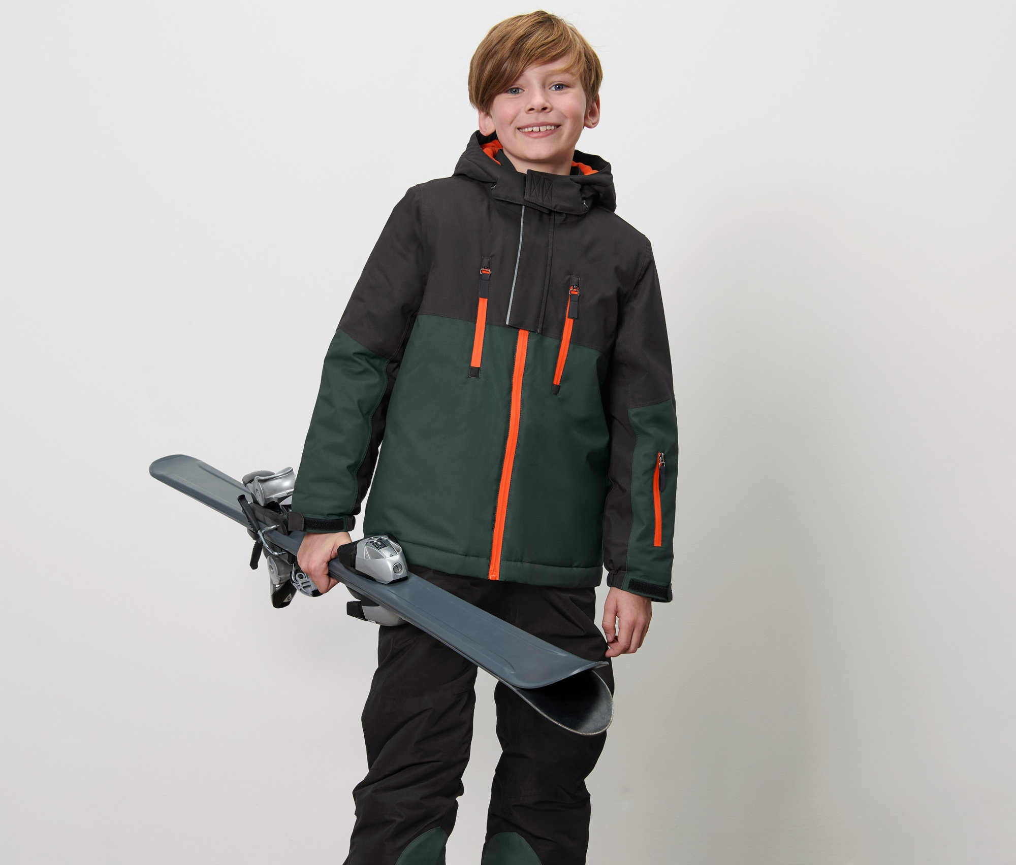 Junge hält Ski und trägt eine Kinder-Skijacke.