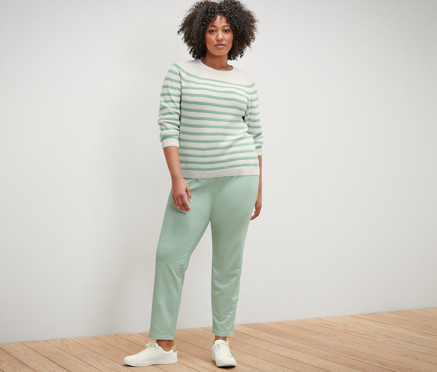 Frau posiert in gestreiftem Strickpullover und Joggpants.