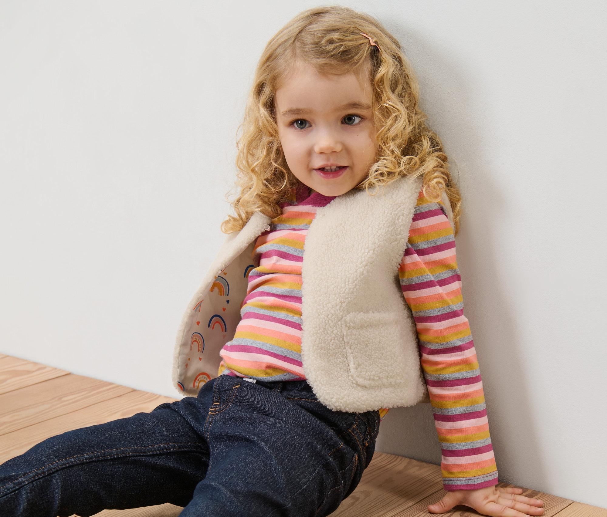 Mädchen sitzt auf dem Boden und trägt eine Kinder-Teddyweste.
