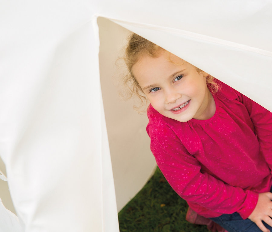 Lächelndes Mädchen schaut aus dem roba Kinderspielzelt »Tipi« heraus.
