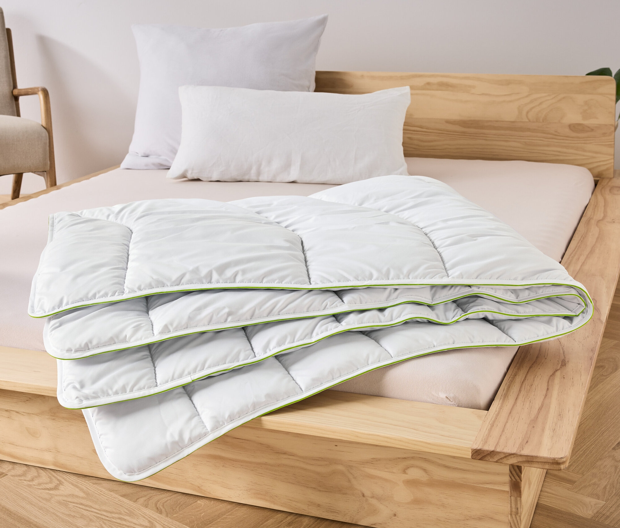 Eine gefaltete irisette® greenline-Steppdecke Dacron®-Aktivkohle liegt auf einem Bett.
