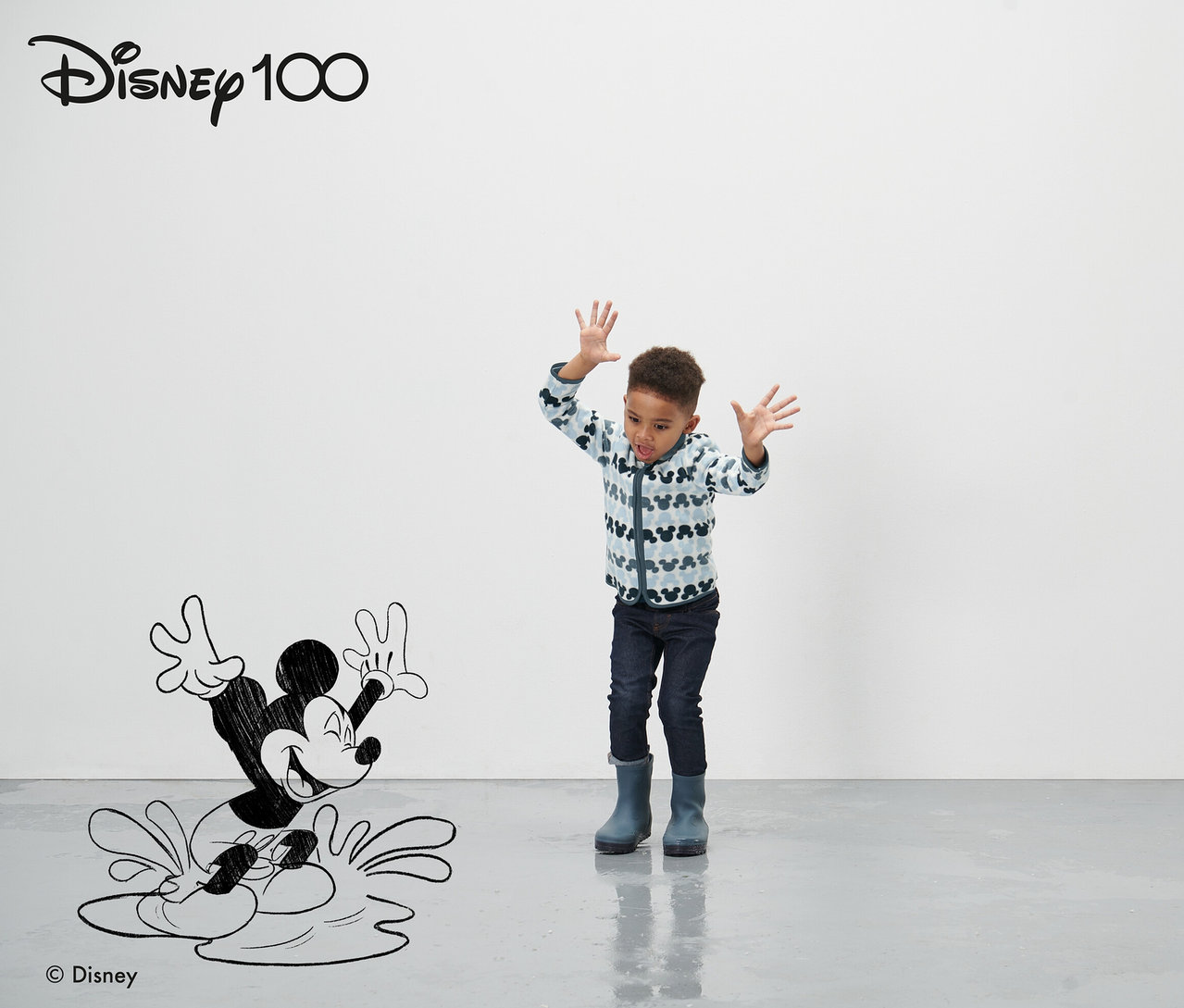 Ein Junge steht vor einer gezeichneten Mickey Mouse Figur und winkt mit seinen Händen. Er trägt eine blaue Kleinkind-Fleecejacke »Micky«.
