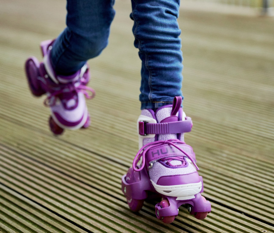 Beine eines Kindes in lavendelfarbenen HUDORA Rollschuhen »My First Quad« in Größe 30–33 auf einem Holzboden.
