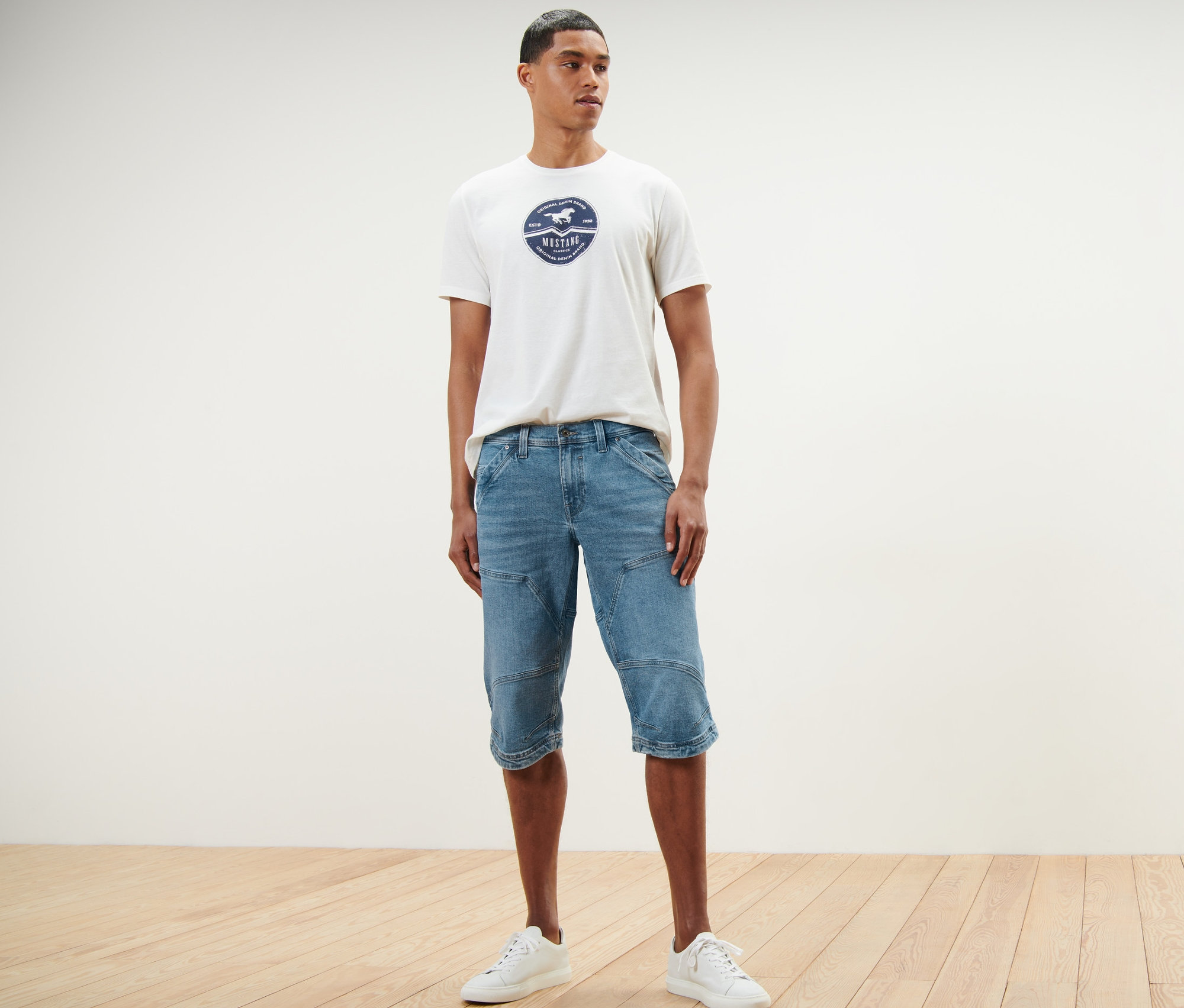 Mann steht und trägt Jeans-Bermuda-Shorts »Mustang« und ein T-Shirt.
