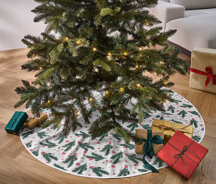Weihnachtsbaum steht auf der Tannenbaumdecke, umgeben von Geschenken.