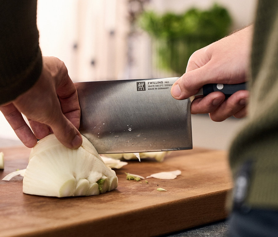 Mann schneidet Fenchelknolle mit ZWILLING PRO Messer auf Holzbrett.