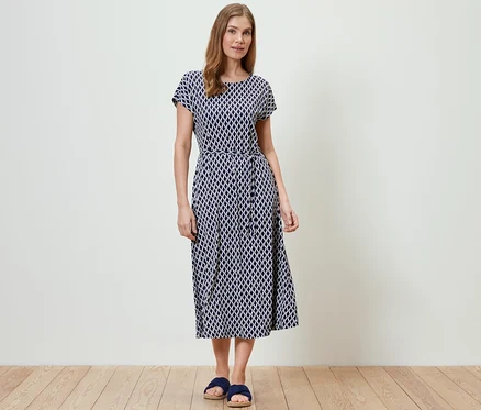 Frau steht und trägt ein bedrucktes Jerseykleid.