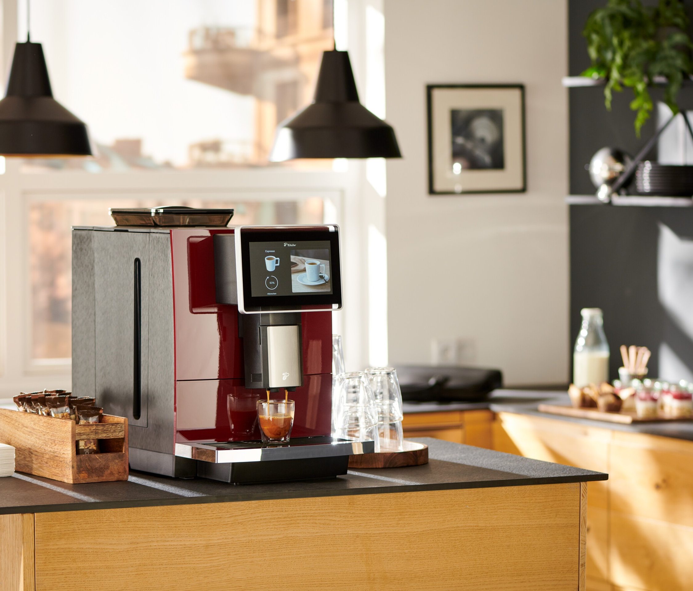 Roter »Tchibo Office« Kaffeevollautomat bereitet Kaffee in ein Glas auf einer Küchentheke zu.