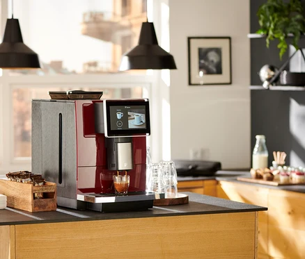 Roter »Tchibo Office« Kaffeevollautomat bereitet Kaffee in ein Glas auf einer Küchentheke zu.