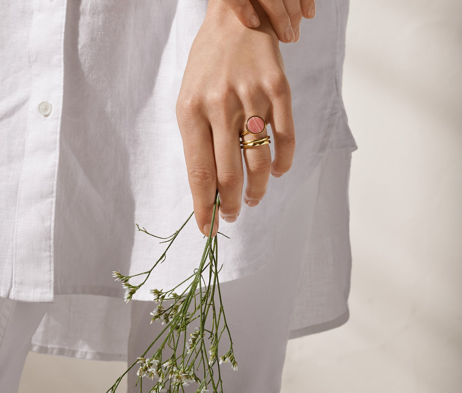 Frau hält 3er-Ring-Set, davon eines 23 Karat vergoldet, und Blumen in der Hand.