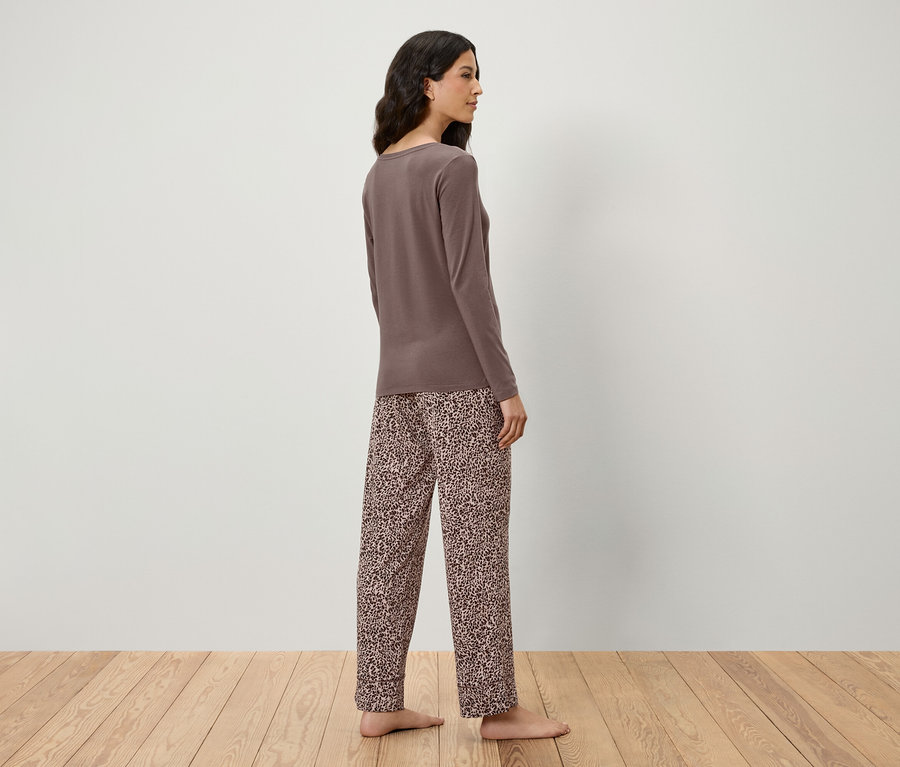 Eine Frau steht seitlich und trägt ein braunes Langarmshirt und eine Hose mit Tiermuster.