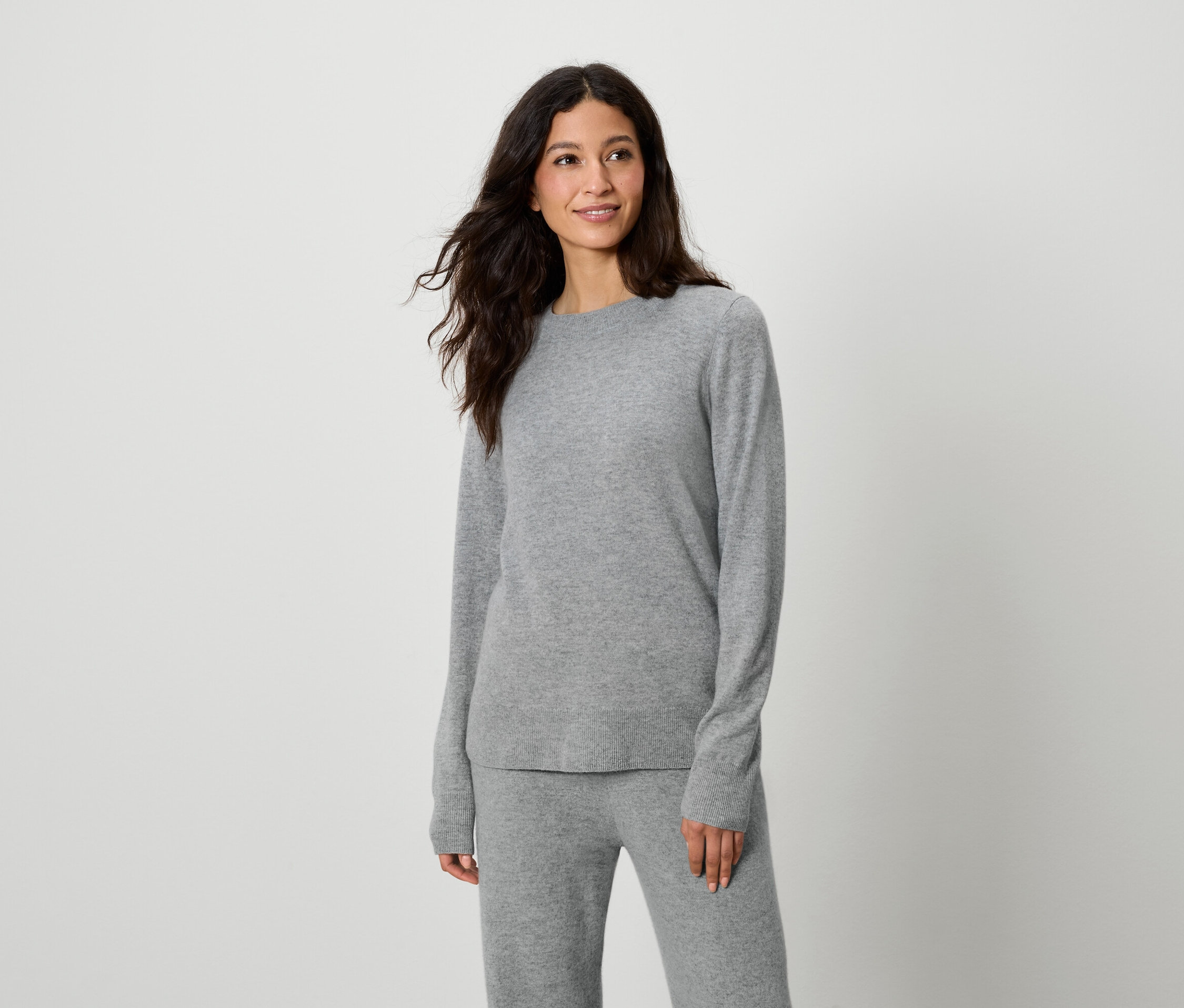 Frau posiert in grauem Pullover und grauer Hose.