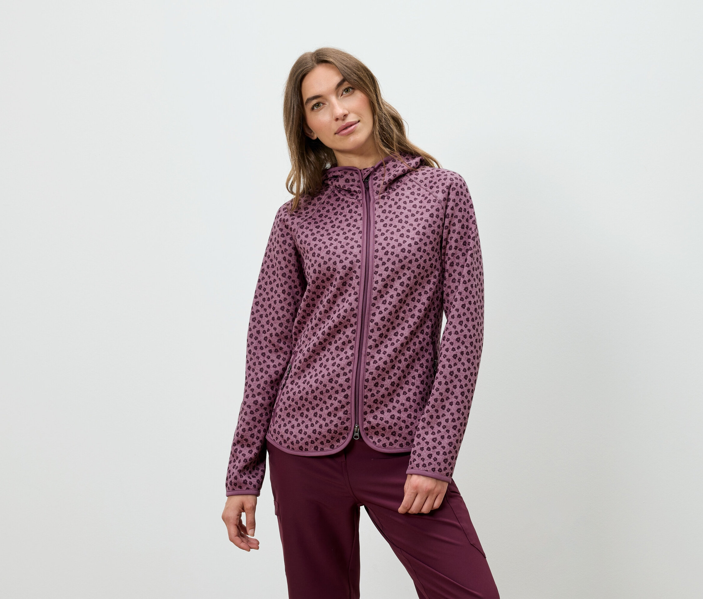 Frau posiert in einem burgunderfarbenen Kapuzenpullover und einer Hose.