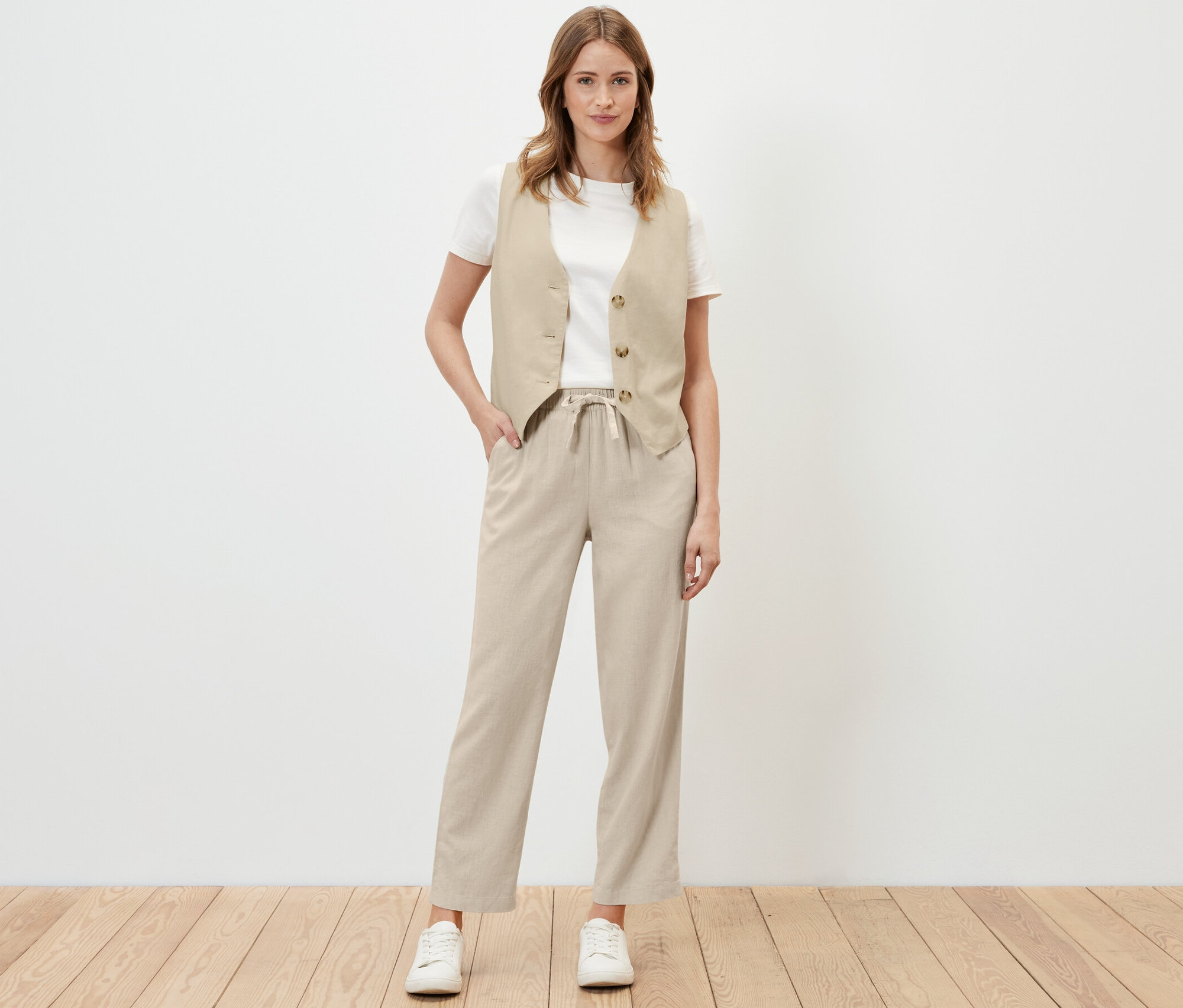 Frau posiert in sandfarbener Leinenhose und Weste.