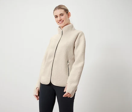 Frau trägt eine cremefarbene Jacke mit schwarzem Reißverschluss und schwarze Leggings.