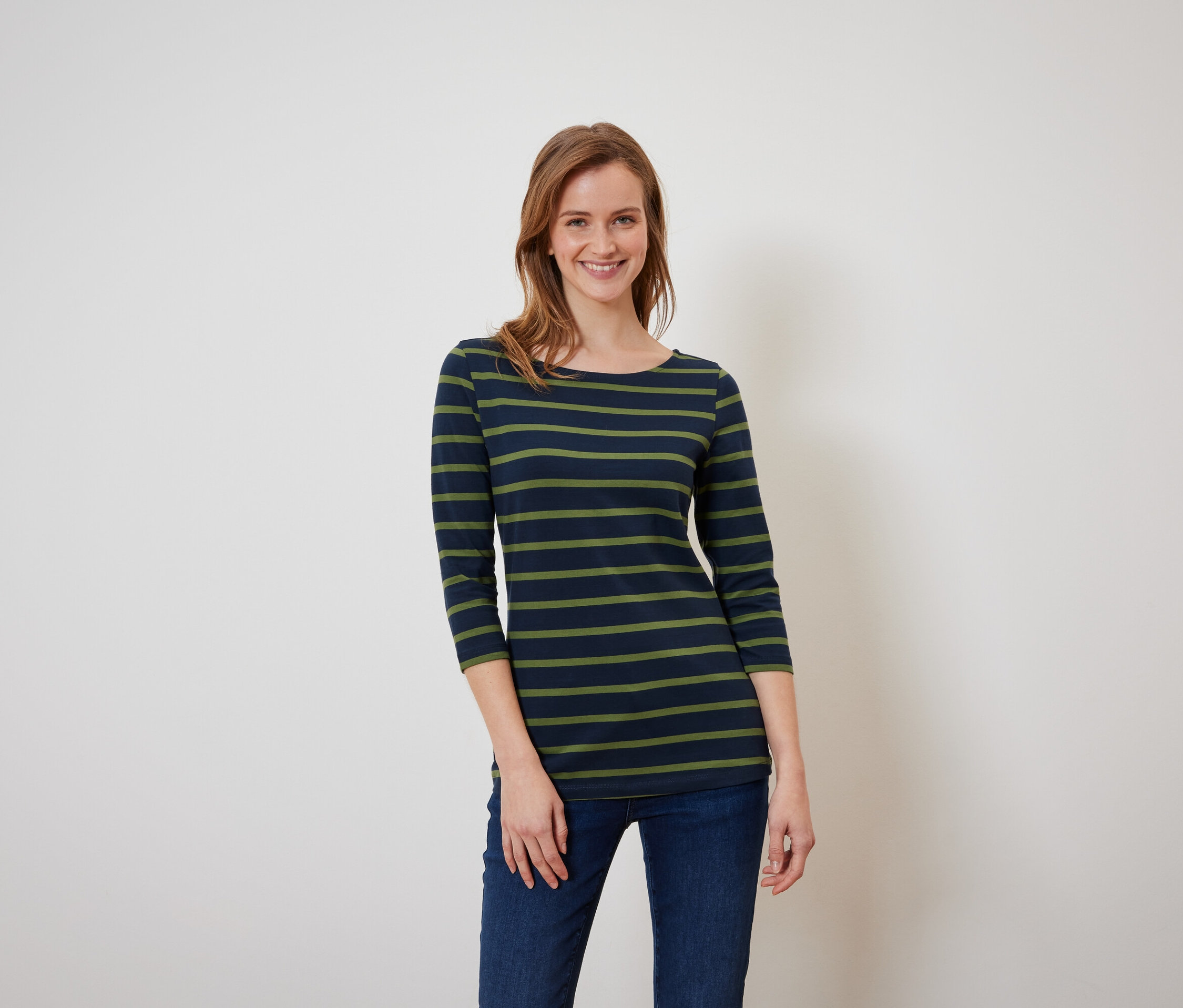 Frau mit braunen Haaren posiert in einem blaugrün gestreiften T-Shirt und blauen Jeans.