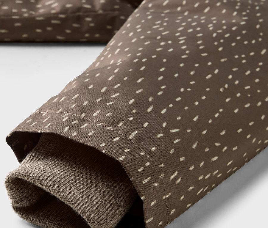 Detail einer Kinder-Thermo-Regenjacke, brauner Stoff mit weißen Punkten und braunem Ärmel.