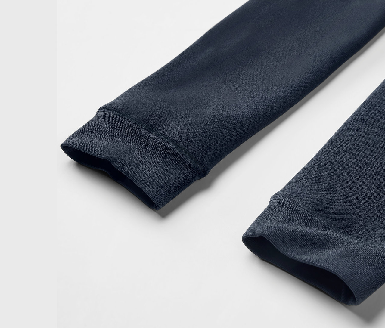 Detailaufnahme von zwei Ärmeln eines dunkelblauen Sweatshirts mit gerippten Bündchen auf weißem Hintergrund.