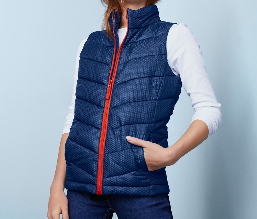 Mädchen trägt eine Steppweste mit recyceltem Material, Jeans und ein Langarmshirt.