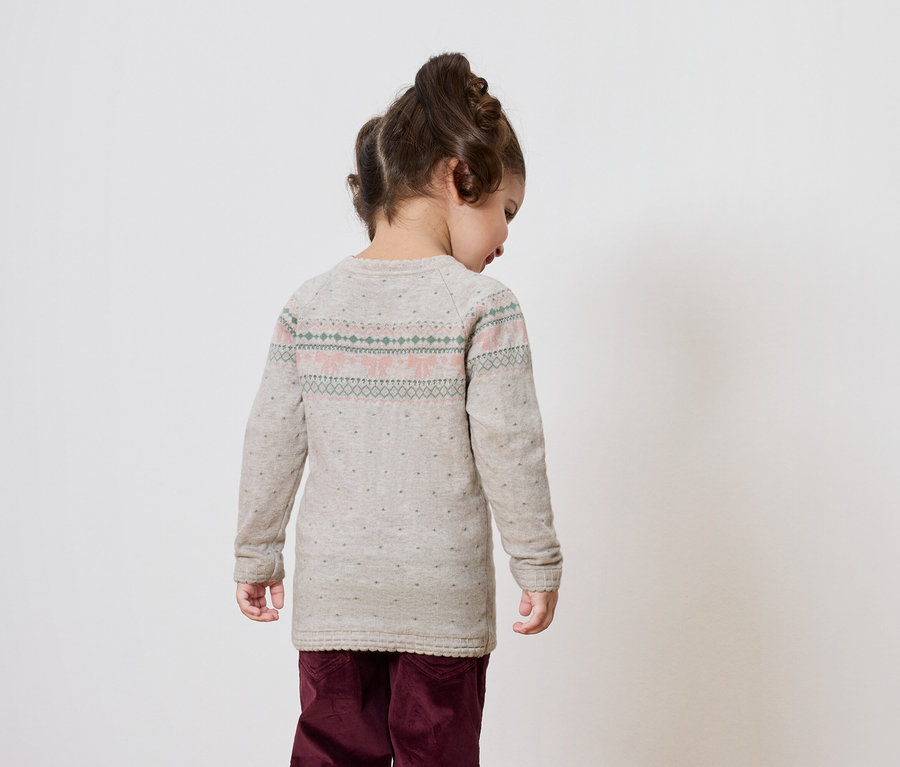 Mädchen mit dem Rücken zur Kamera in grauem Pullover und weinroter Hose.